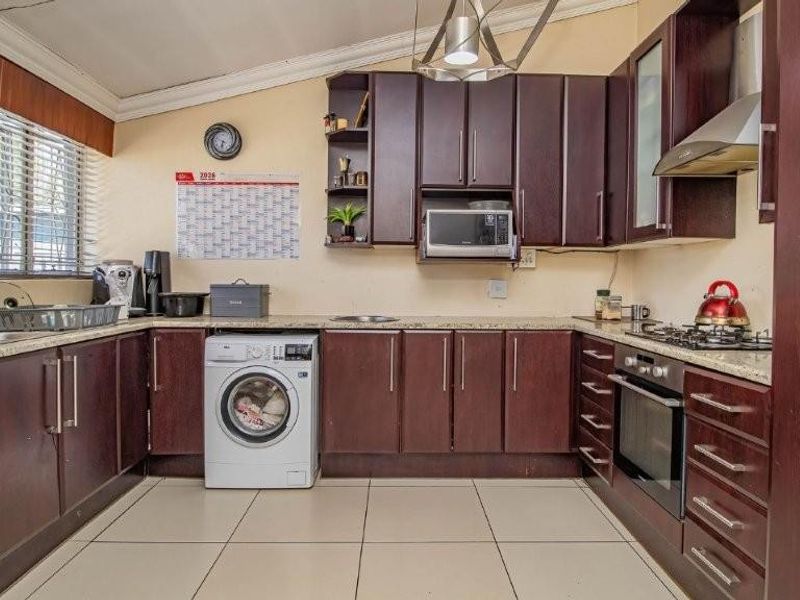 A functional kitchen featuring dark wood cabinetry, granite countertops, built-in oven with gas hob, and an integrated washing machine.