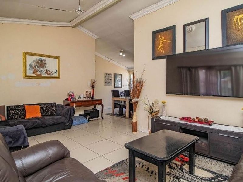 Spacious living room featuring tiled flooring and coved ceilings, with visible wall and ceiling maintenance required.