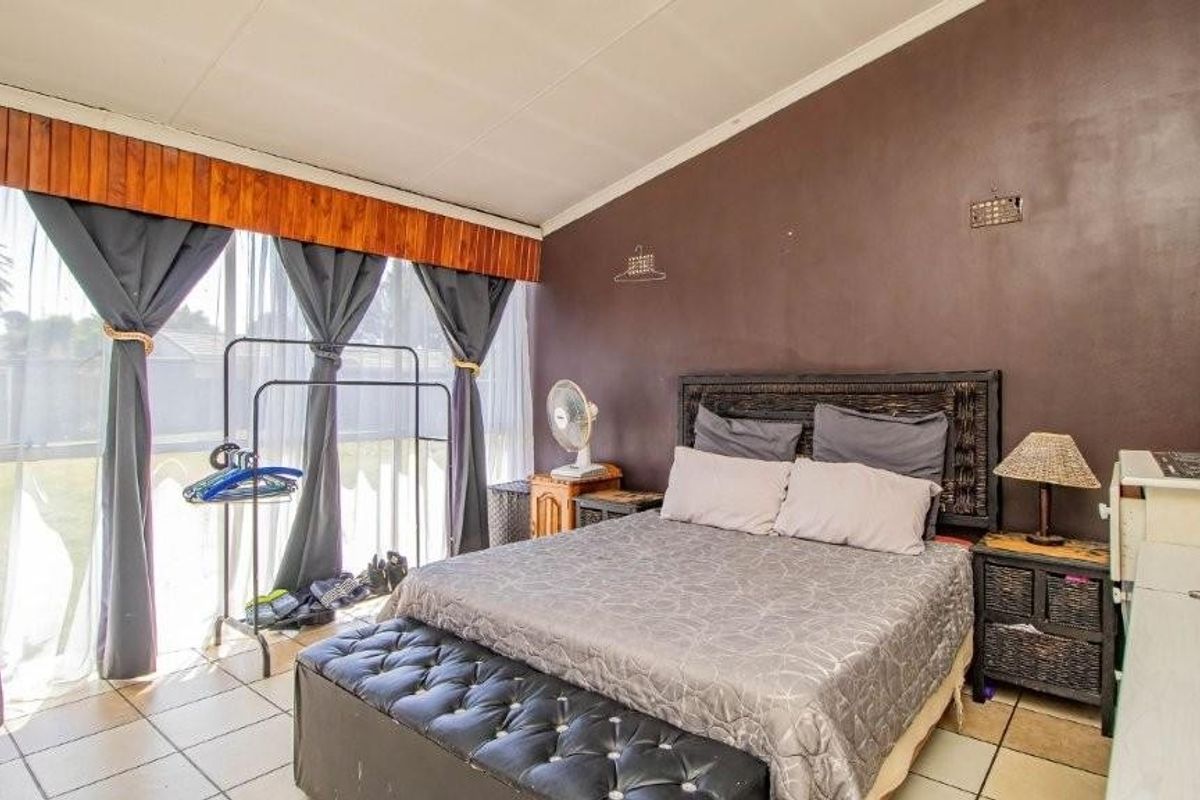 A bedroom featuring tiled flooring, a sloped ceiling, and a large sliding glass door providing natural light.
