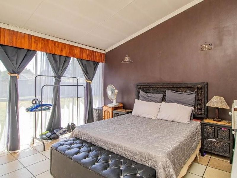 A bedroom featuring tiled flooring, a sloped ceiling, and a large sliding glass door providing natural light.