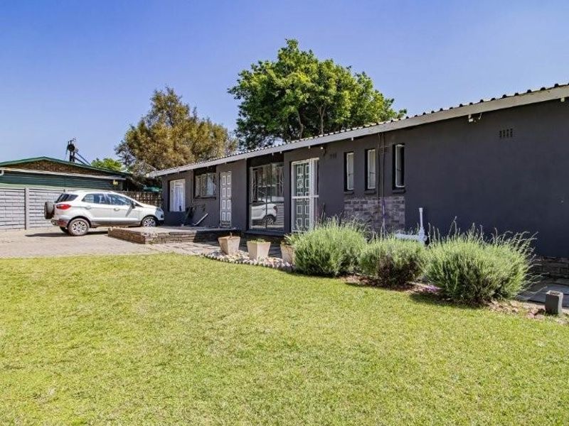 Rear view of the property featuring a paved driveway, lawn area, and security gates leading into the home.