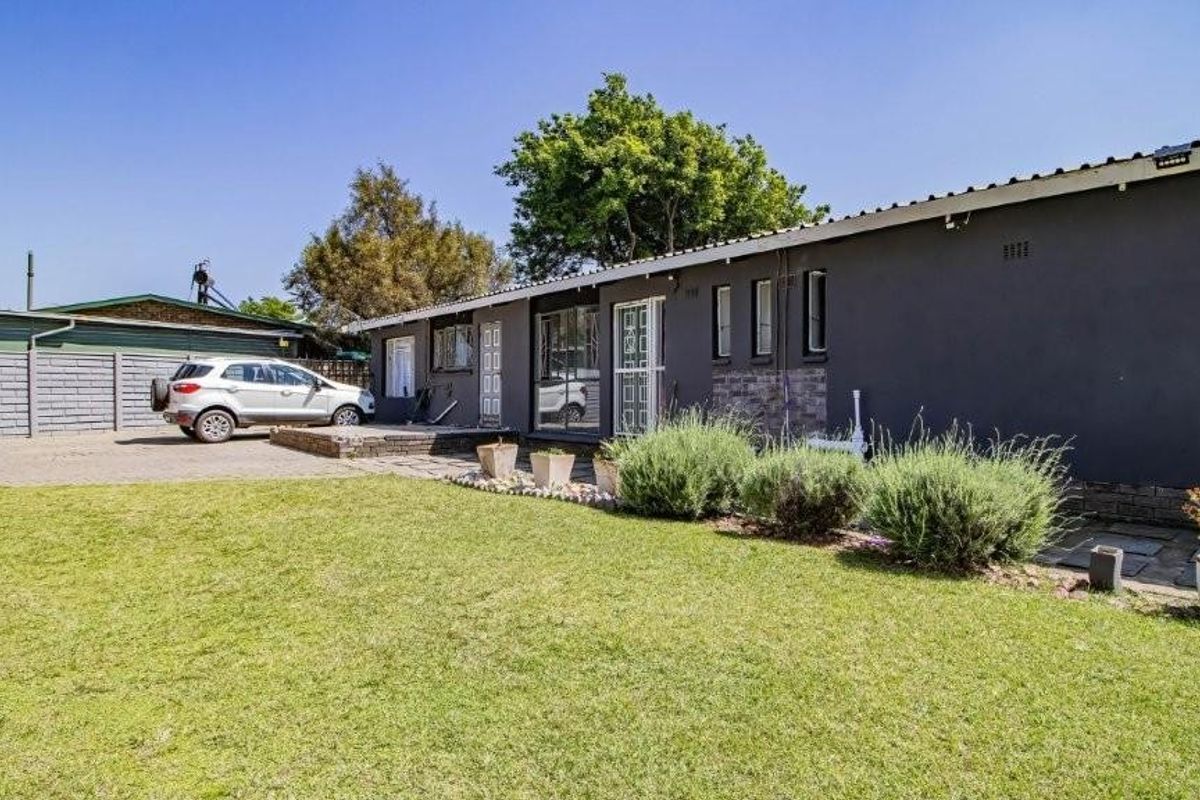 Rear view of the property featuring a paved driveway, lawn area, and security gates leading into the home.