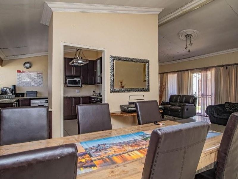 Open-plan living and dining area featuring tiled floors, ceiling detailing, and an adjacent kitchen with built-in cabinetry and appliances.