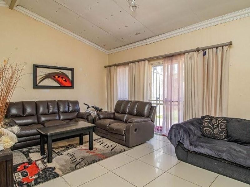 A living room featuring tiled flooring and a sliding glass door leading to the exterior, with visible wear on the walls and ceiling.