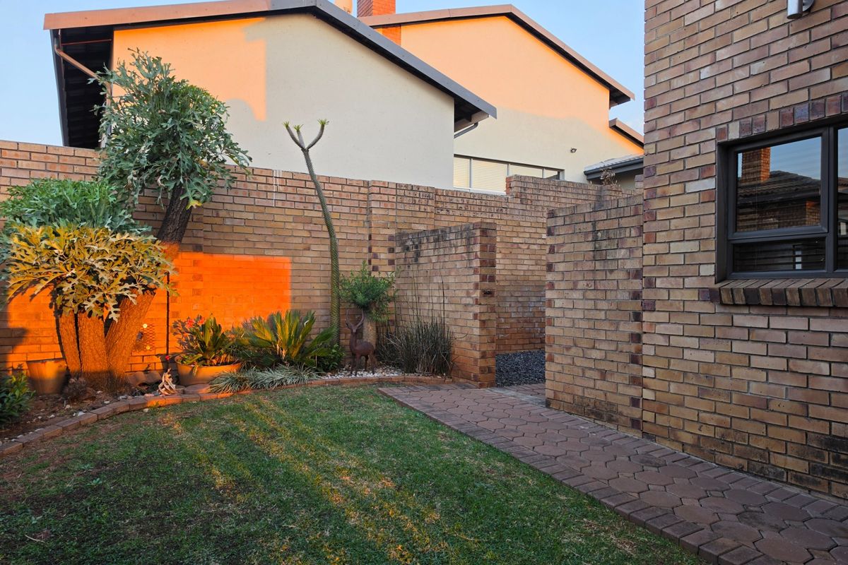 A well-maintained rear garden area featuring face brick boundary walls, a paved walkway, and established landscaping at sunset.