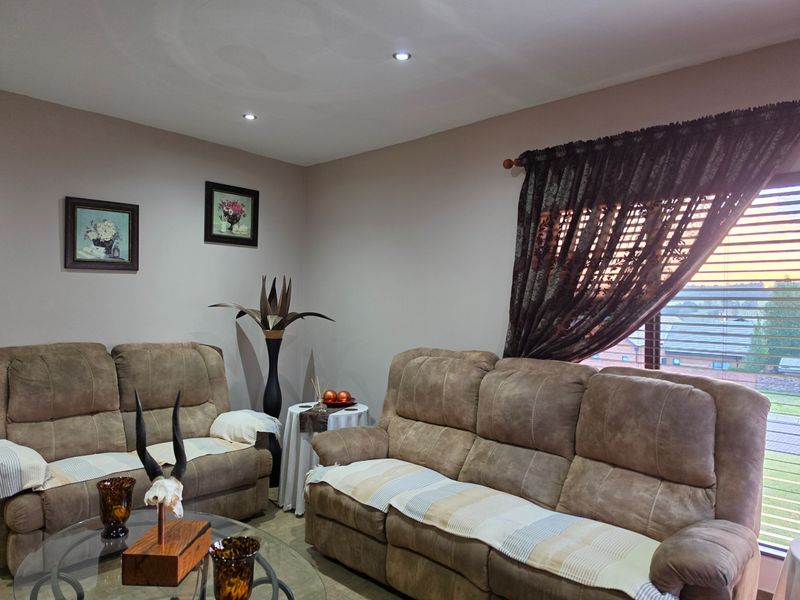 A comfortable living room featuring recessed downlighting and large windows with venetian blinds and decorative curtains.