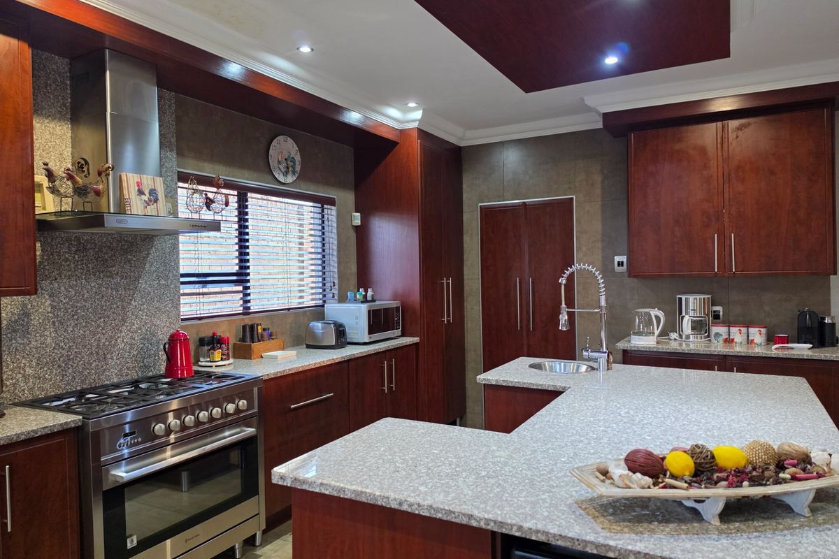 Modern kitchen featuring dark wood cabinetry, granite countertops, a central island with a sink, and high-end stainless steel gas stove and extractor fan.