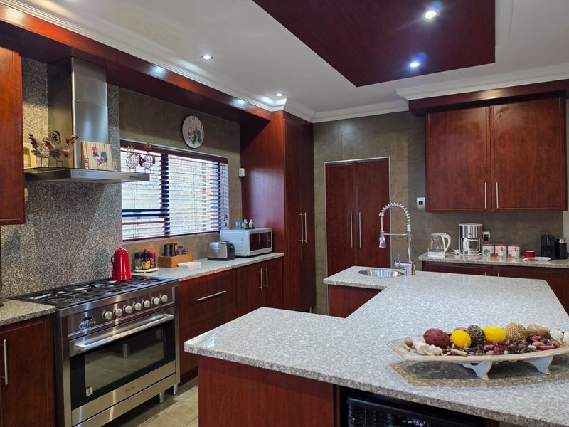 Modern kitchen featuring dark wood cabinetry, granite countertops, a central island with a sink, and high-end stainless steel gas stove and extractor fan.