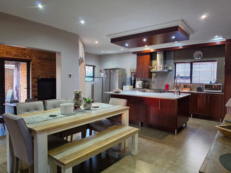 Spacious open-plan kitchen and dining area featuring a central island, dark wood cabinetry, recessed lighting, and an adjacent brick-accented living space with a fireplace.
