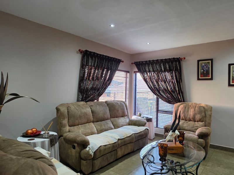 A comfortable living room featuring tiled flooring, recessed downlighting, and large windows fitted with venetian blinds and decorative curtains.