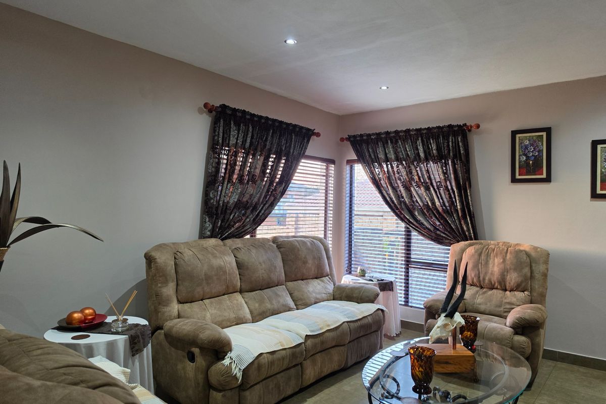 A comfortable living room featuring tiled flooring, recessed downlighting, and large windows fitted with venetian blinds and decorative curtains.