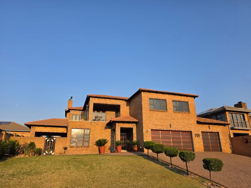 A well-maintained double-story brick house featuring a tiled roof, double garage, paved driveway, and an upper-level balcony.
