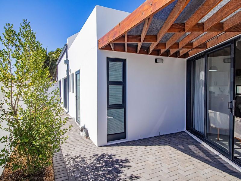 A modern paved patio area featuring a timber pergola and large sliding glass doors providing seamless indoor-outdoor flow.