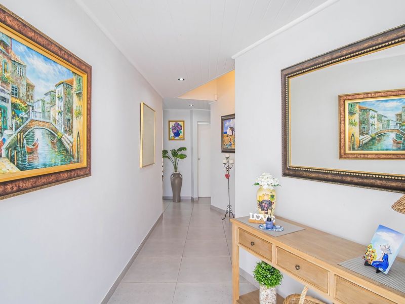 A bright and well-maintained hallway featuring neutral tiled flooring, recessed downlighting, and a clean tongue and groove ceiling finish.