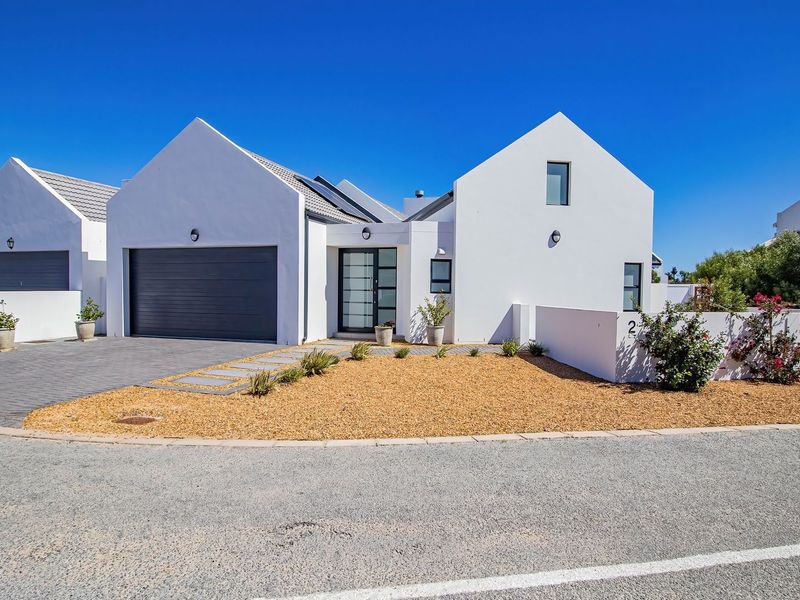 Modern single-story house featuring a gabled roof, double garage, paved driveway, and clean white exterior finishes with solar panels.