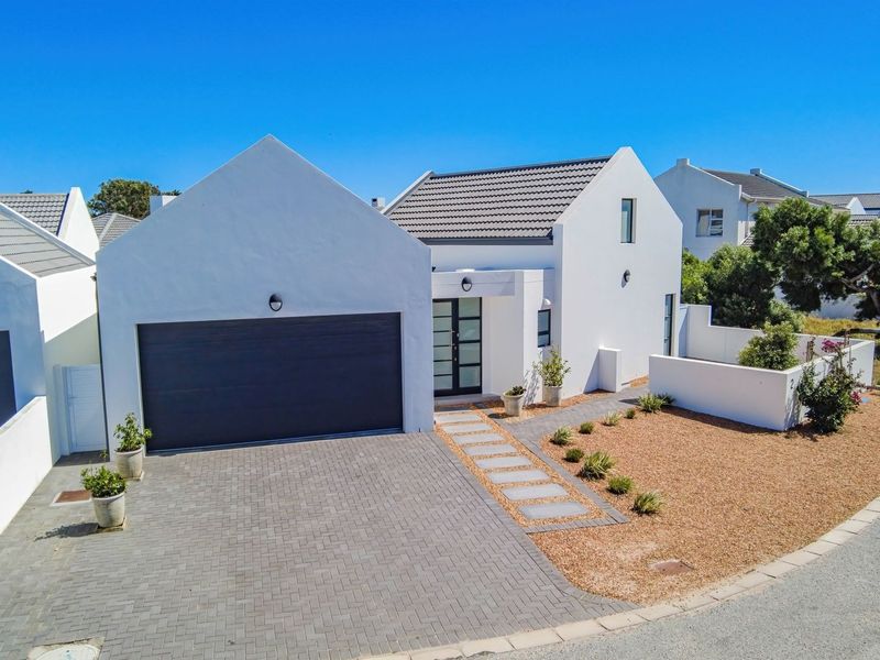 Modern single-story home featuring a clean white facade, double garage, paved driveway, and a landscaped front garden with a stone walkway.