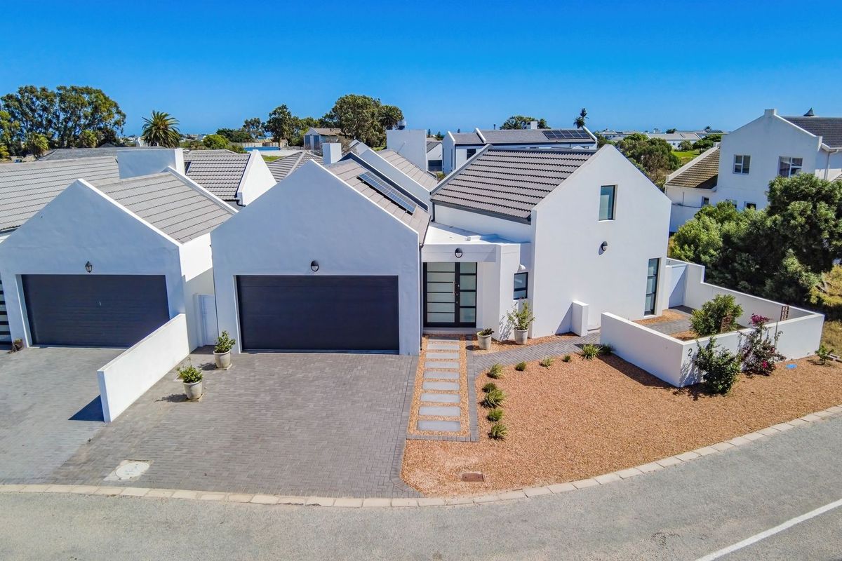 Aerial view of a modern residential property featuring a tiled roof, paved driveway, double garage, and landscaped front garden area.
