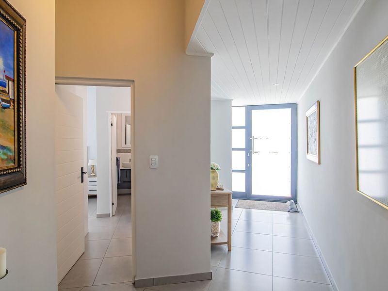A bright and welcoming entrance hallway featuring tiled flooring, a tongue and groove ceiling, and a modern glass-panelled front door.
