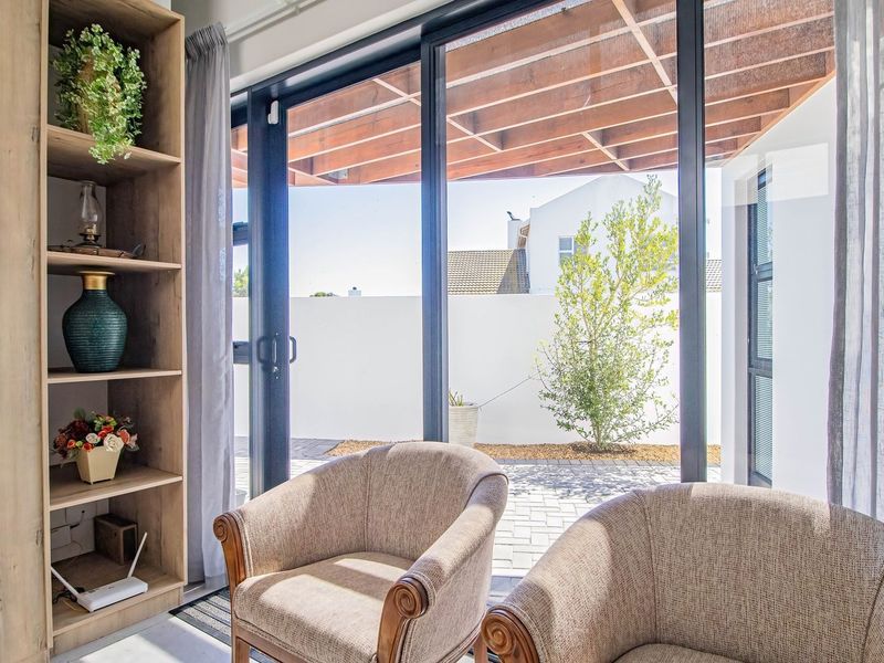 A bright living area featuring a built-in wooden shelving unit and large sliding glass doors that open onto a paved patio with a timber pergola.