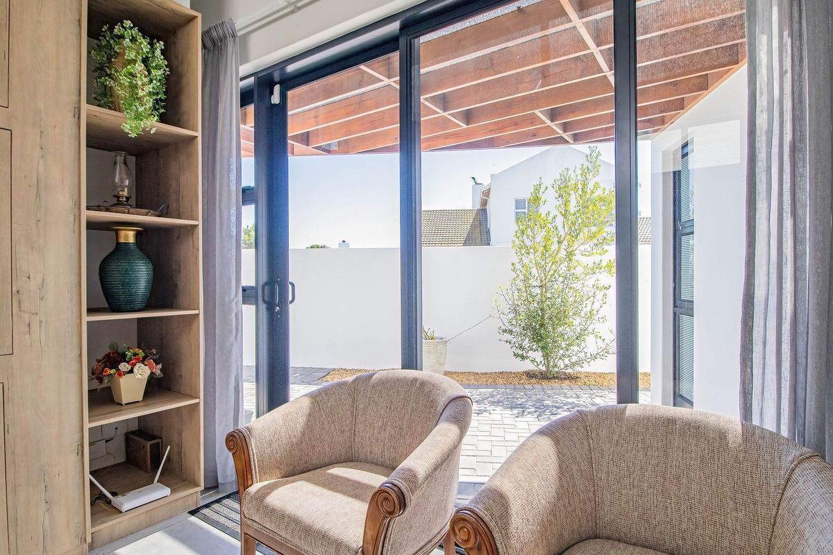 A bright living area featuring a built-in wooden shelving unit and large sliding glass doors that open onto a paved patio with a timber pergola.