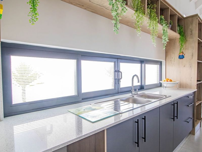 Modern kitchen featuring sleek dark cabinetry, quartz countertops, a stainless steel sink, and integrated open shelving with a bright, contemporary aesthetic.