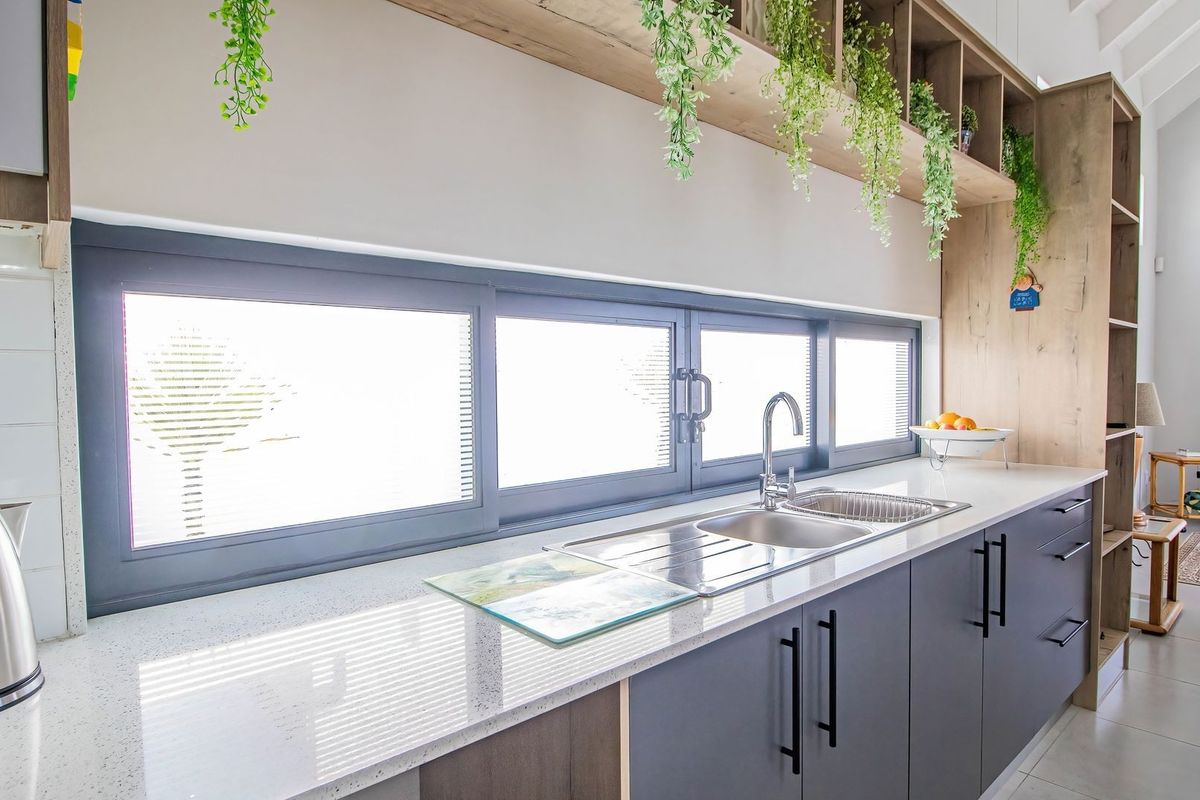 Modern kitchen featuring sleek dark cabinetry, quartz countertops, a stainless steel sink, and integrated open shelving with a bright, contemporary aesthetic.