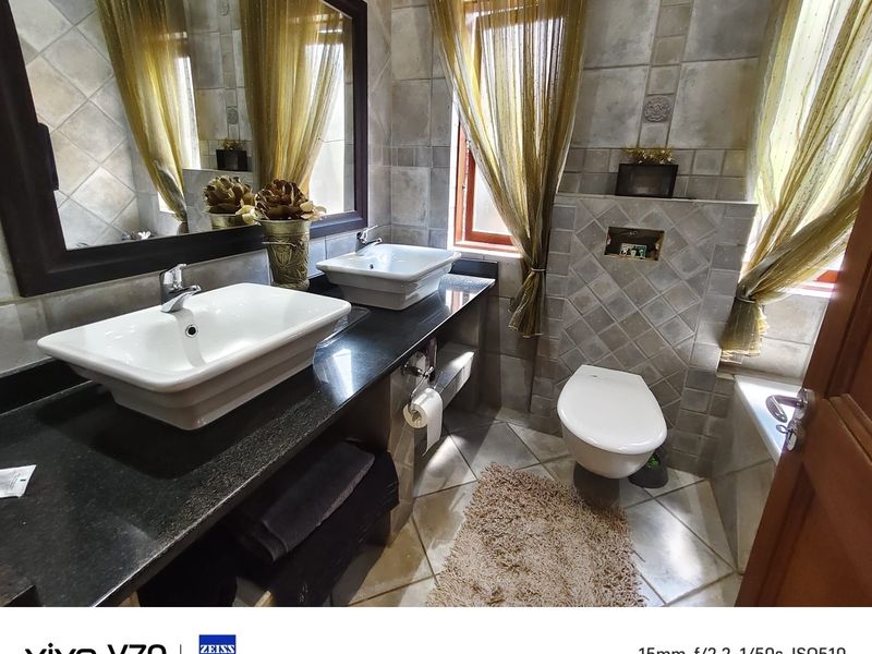 A well-appointed bathroom featuring a double vanity with vessel sinks, granite countertops, and a wall-mounted toilet with neutral tiled finishes.