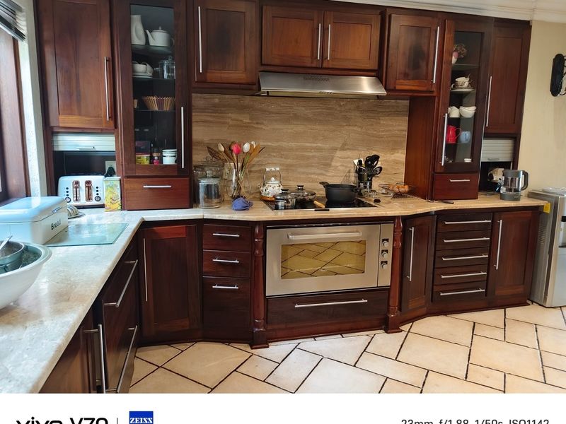 A well-maintained kitchen featuring dark wood cabinetry, stone countertops, a stone backsplash, and integrated stainless steel appliances with stone tile flooring.