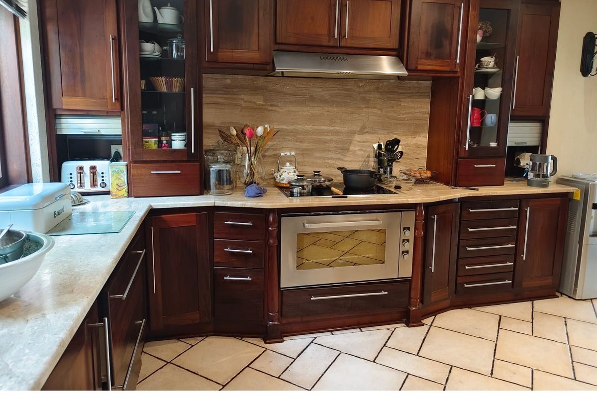A well-maintained kitchen featuring dark wood cabinetry, stone countertops, a stone backsplash, and integrated stainless steel appliances with stone tile flooring.