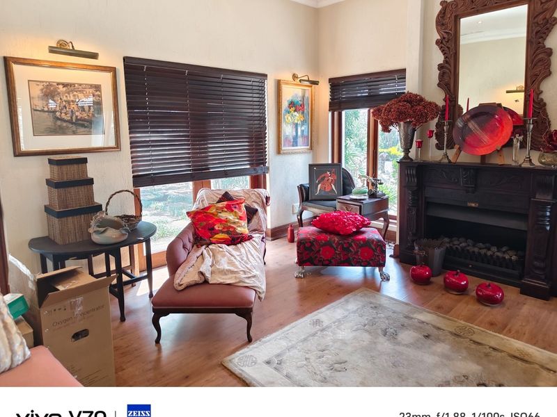 A cozy living room featuring a traditional fireplace with an ornate mantelpiece, timber flooring, and large windows with venetian blinds.
