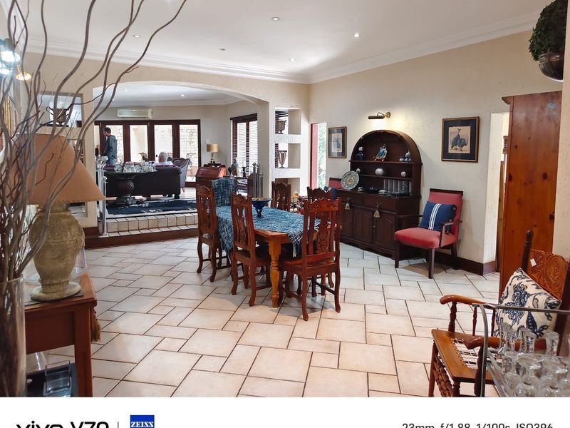 Spacious open-plan dining area featuring tiled flooring, recessed lighting, and an arched transition leading to an adjacent living space with glass doors.