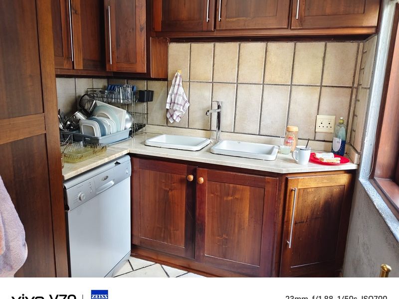 Compact scullery area featuring dark wood cabinetry, double basin sink, and tiled splashback, providing functional prep and wash-up space.