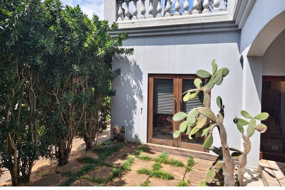 Rear exterior view featuring a stone paved patio area, double glass doors, and a decorative balustrade on the upper level.