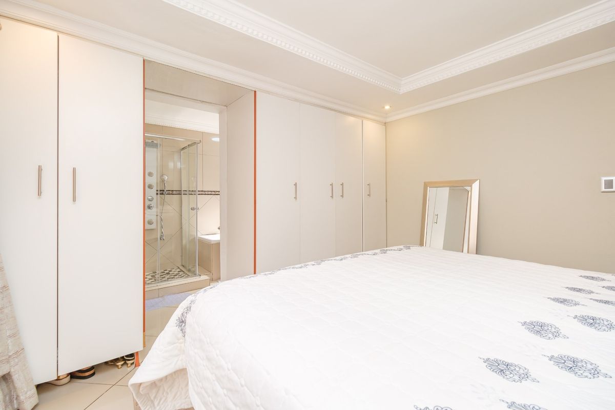 A well-maintained bedroom featuring extensive built-in wardrobes, elegant crown molding, and an adjoining en-suite bathroom with a glass-enclosed shower.