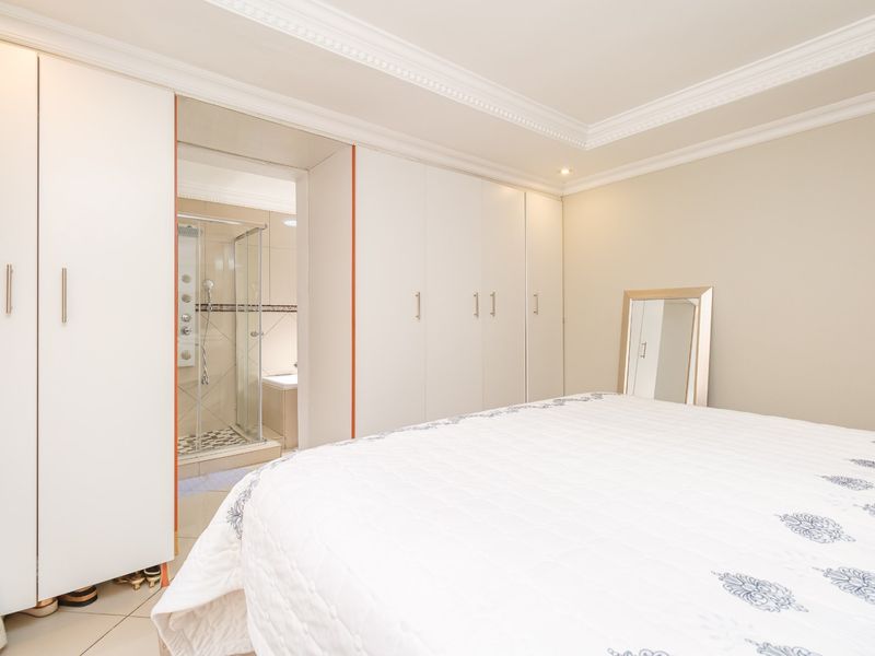 A well-maintained bedroom featuring extensive built-in wardrobes, elegant crown molding, and an adjoining en-suite bathroom with a glass-enclosed shower.