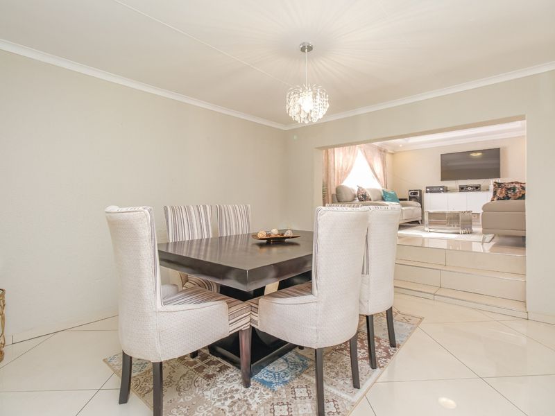 Open-plan dining area featuring tiled flooring and a split-level transition into the adjacent living space, illuminated by a modern pendant light fixture.