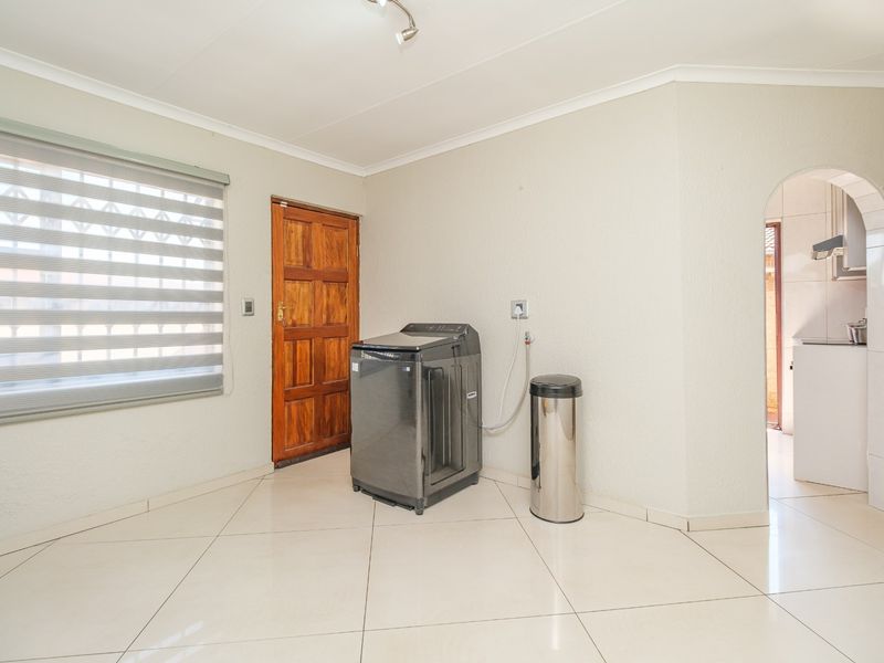 A clean, functional laundry area featuring tiled flooring, a wooden exterior door, and an arched entryway leading to the kitchen.