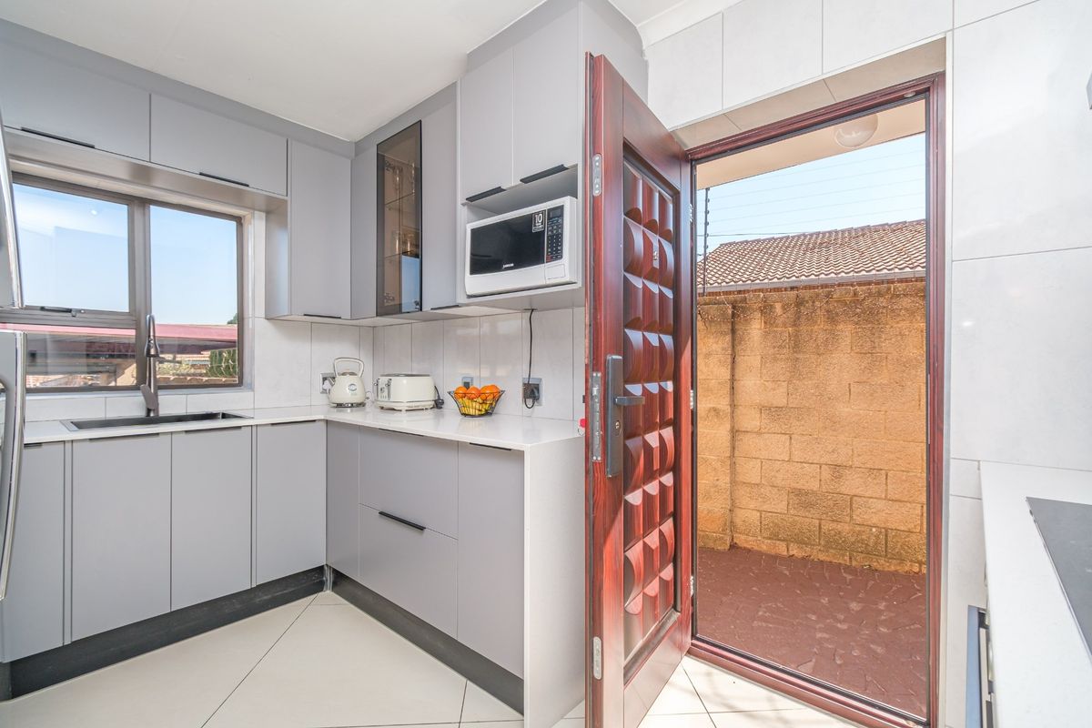 Modern kitchen featuring sleek grey cabinetry, stone countertops, integrated microwave, and direct access to an outdoor area through a solid wood door.