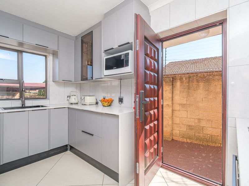 Modern kitchen featuring sleek grey cabinetry, stone countertops, integrated microwave, and direct access to an outdoor area through a solid wood door.
