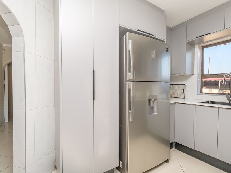 A modern kitchen featuring light grey cabinetry, tiled flooring, a stainless steel sink, and an arched entryway leading to adjacent living spaces.