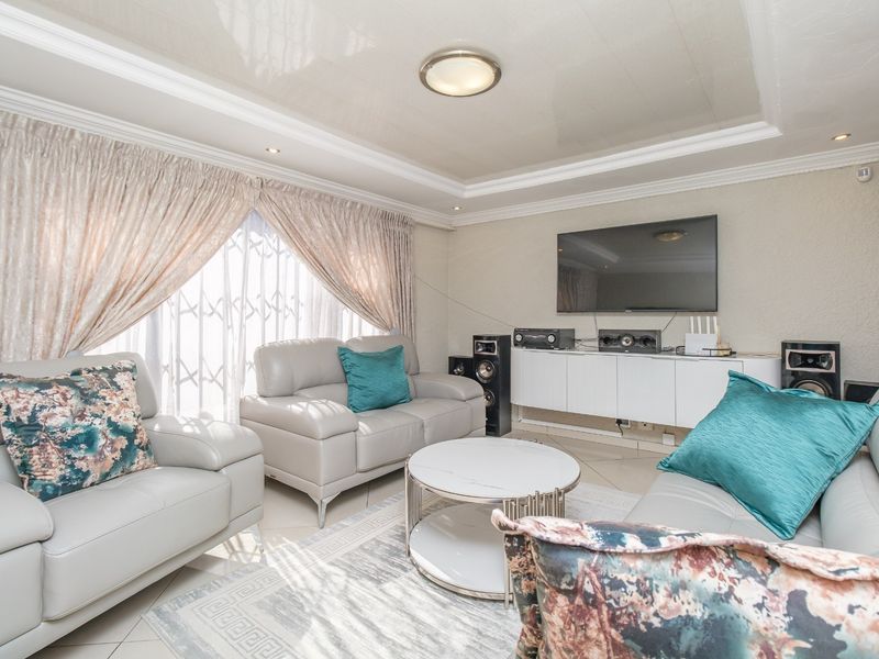 A well-maintained living room featuring tiled flooring, a recessed ceiling with cove lighting, and a secure window treatment.