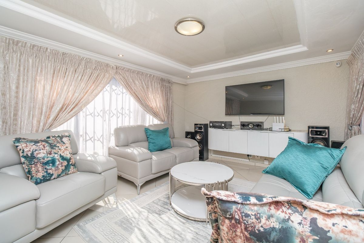 A well-maintained living room featuring tiled flooring, a recessed ceiling with cove lighting, and a secure window treatment.