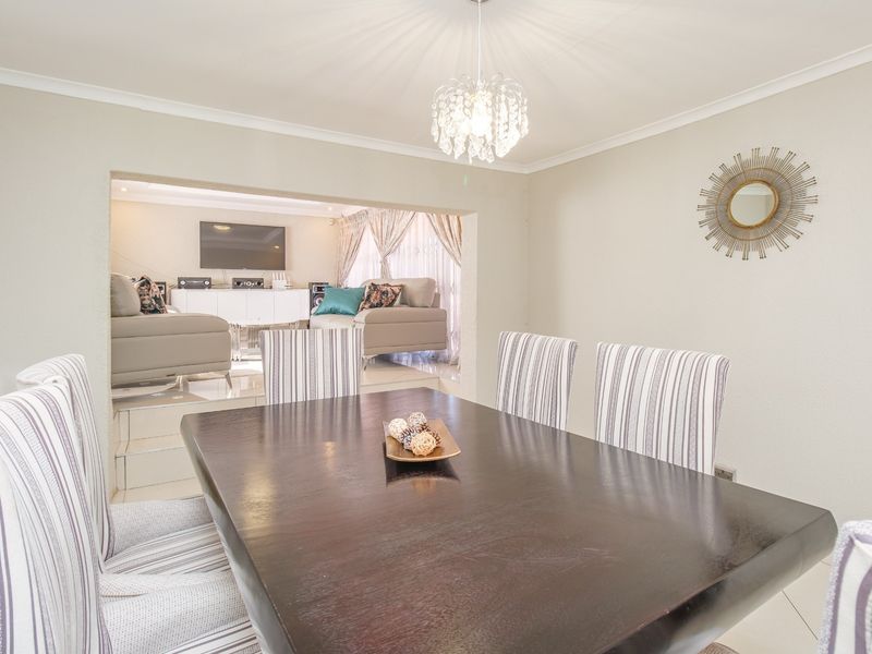 An open-plan dining area featuring tiled flooring, a decorative crystal chandelier, and a raised transition leading into the adjacent living space.