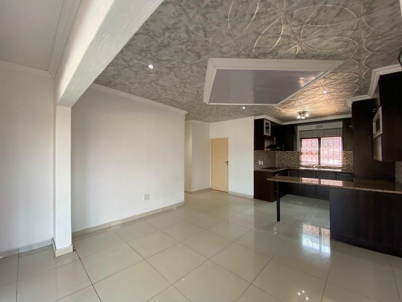 Spacious open-plan living and kitchen area featuring tiled floors, modern dark cabinetry, granite countertops, and unique decorative ceiling detailing.