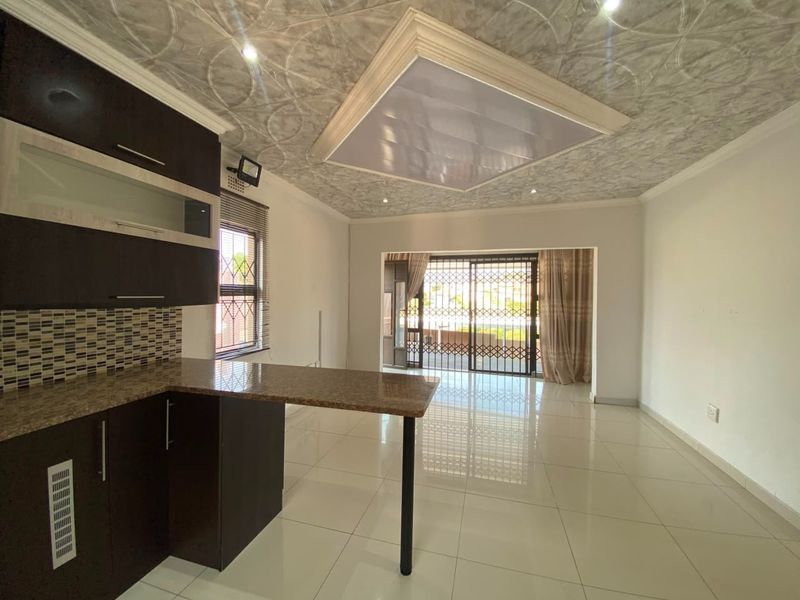 Spacious open-plan living area featuring a modern kitchen with granite countertops, tiled floors, and direct access to an outdoor patio through security gates.