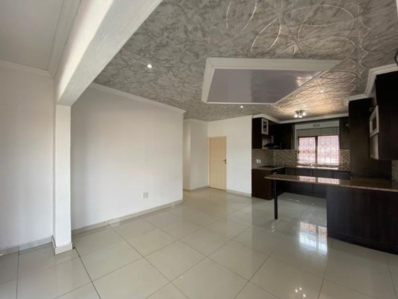 Spacious open-plan living and kitchen area featuring tiled floors, modern dark cabinetry, granite countertops, and unique decorative ceiling finishes.