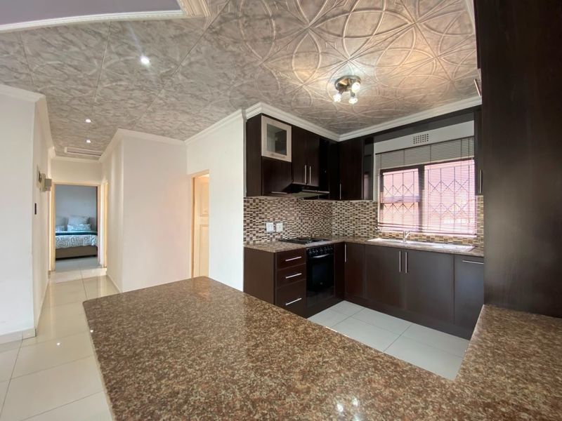 Modern kitchen featuring dark cabinetry, granite countertops, built-in oven and hob, and unique decorative ceiling tiles, with an open-plan layout.