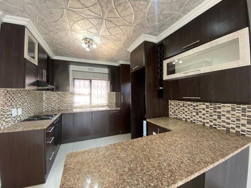 A well-maintained kitchen featuring dark wood cabinetry, granite countertops, a mosaic tile backsplash, and unique decorative ceiling tiles.