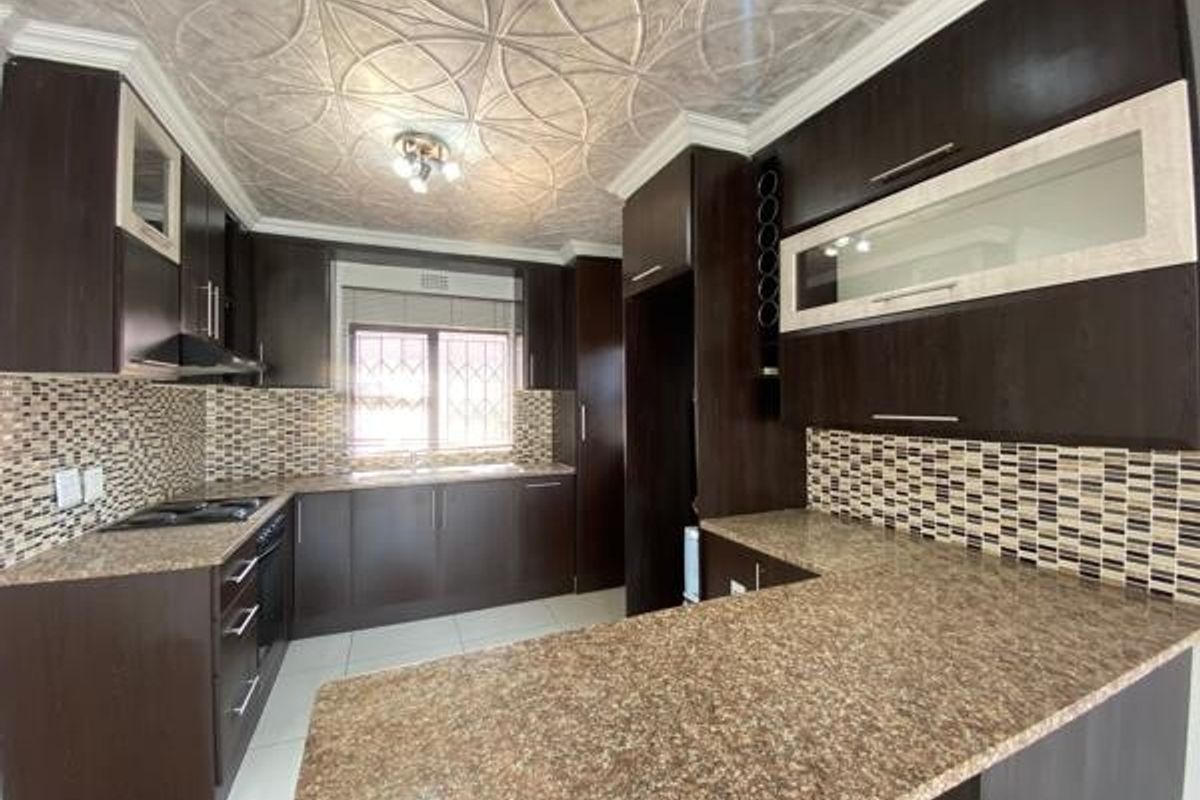 A well-maintained kitchen featuring dark wood cabinetry, granite countertops, a mosaic tile backsplash, and unique decorative ceiling tiles.