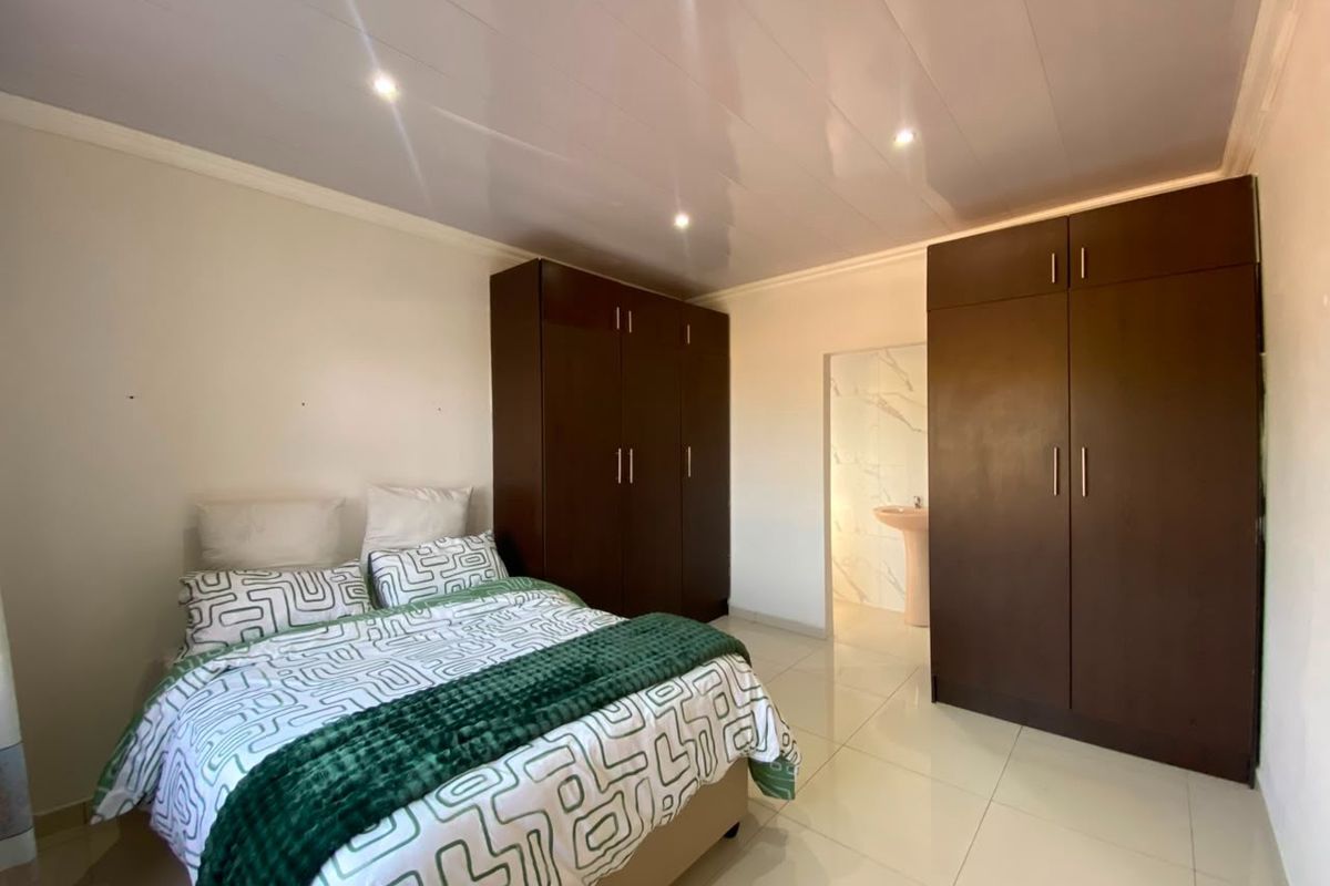 A well-maintained bedroom featuring tiled flooring, recessed ceiling lighting, and ample built-in cupboard storage, with an adjoining en-suite bathroom visible.